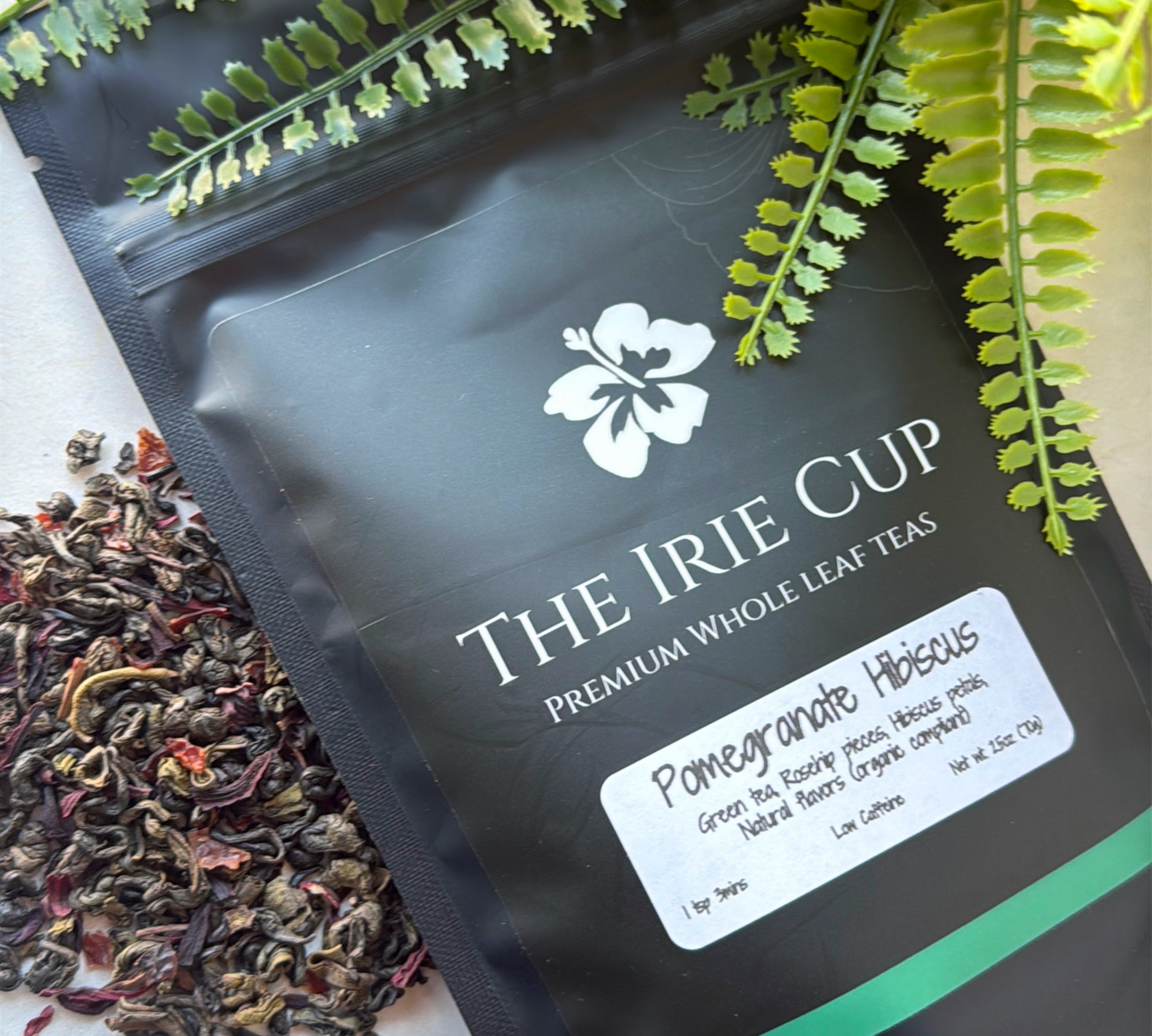 A package of 'The Irie Cup' Pomegranate Hibiscus tea with dried leaves and pieces of pomegranate visible in the foreground.