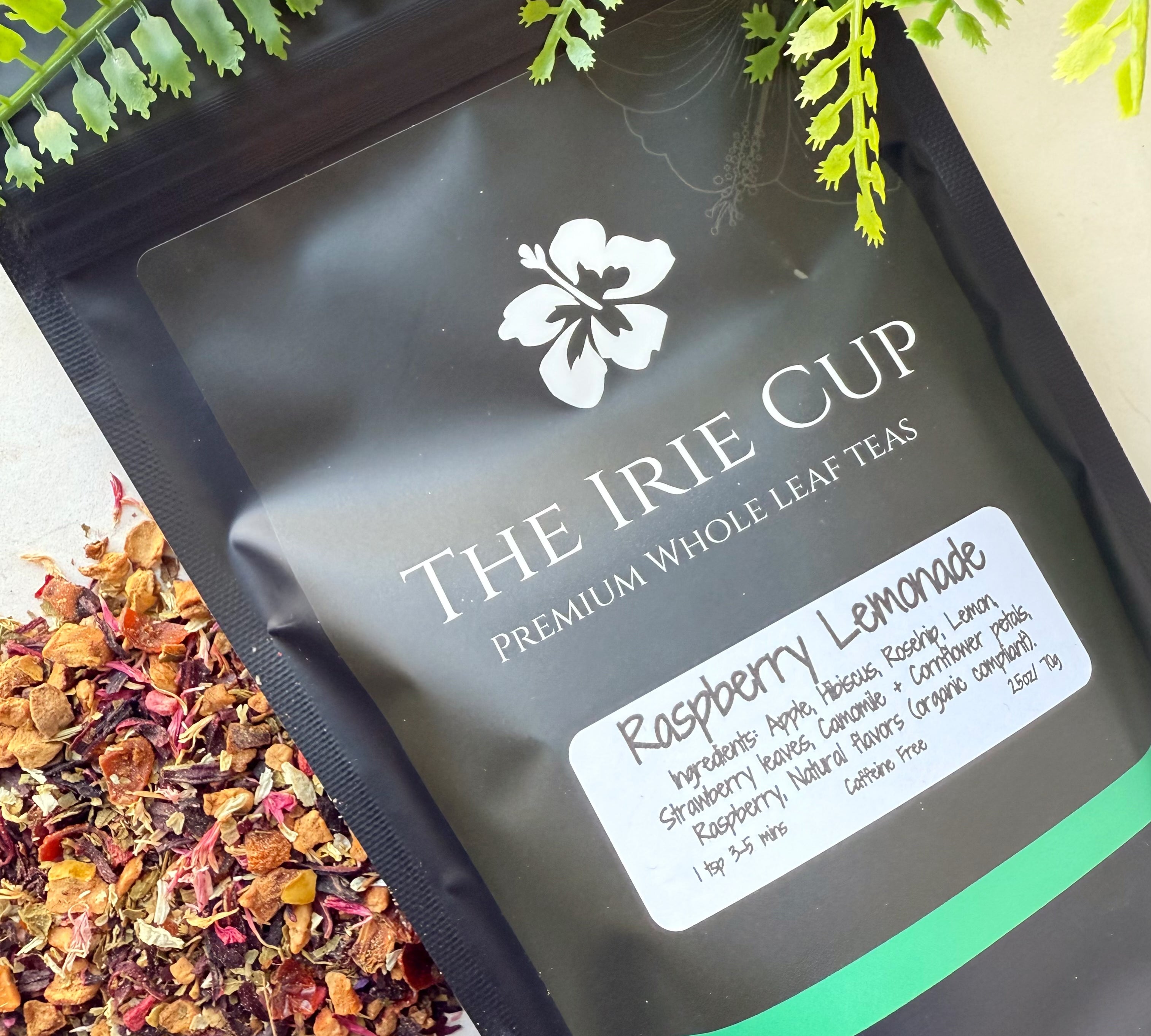 A package of 'The Irie Cup' Raspberry Lemonade tea with loose tea leaves and pieces of raspberry and hibiscus visible in the foreground.
