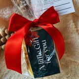 Gift bag with red ribbon and 'A Little Gift for You' tag on a textured surface