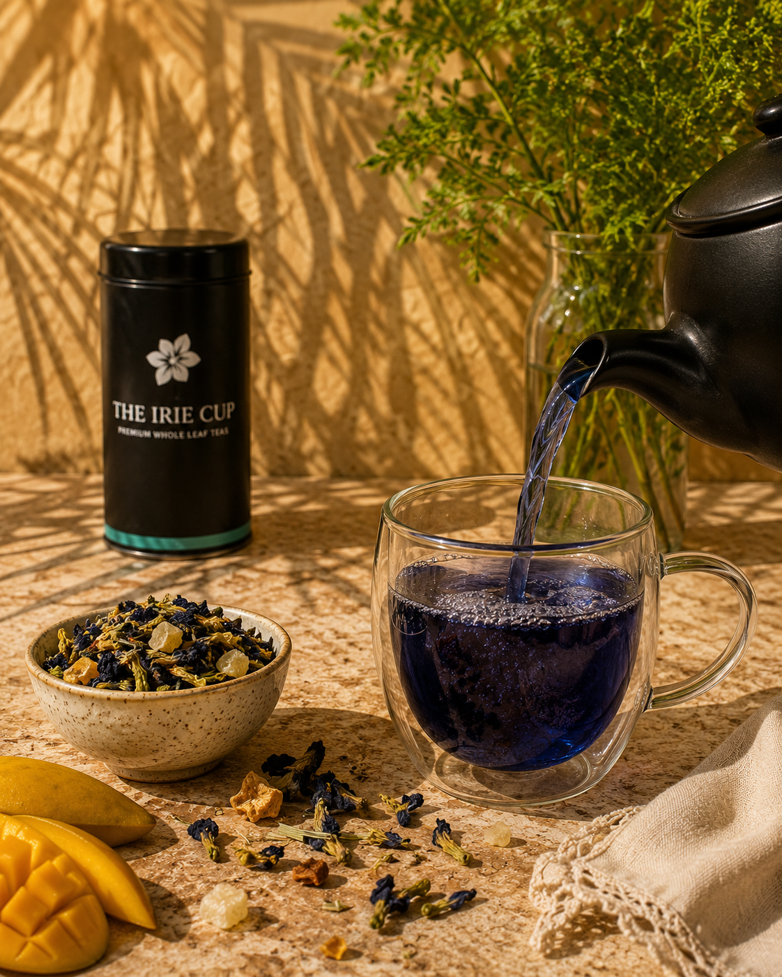 Tea being poured into a glass mug with tea leaves and a container labeled 'The Irie Cup' on a wooden surface.