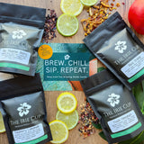 Multiple packaged tea bags from 'The Irie Cup' displayed on a wooden surface with fruits and tea leaves around them, indicating flavors like peach, lemon, and berry.