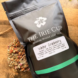 Tea package labeled 'The Irie Cup' with a sample of winter cranberry tea leaves on a wooden surface.