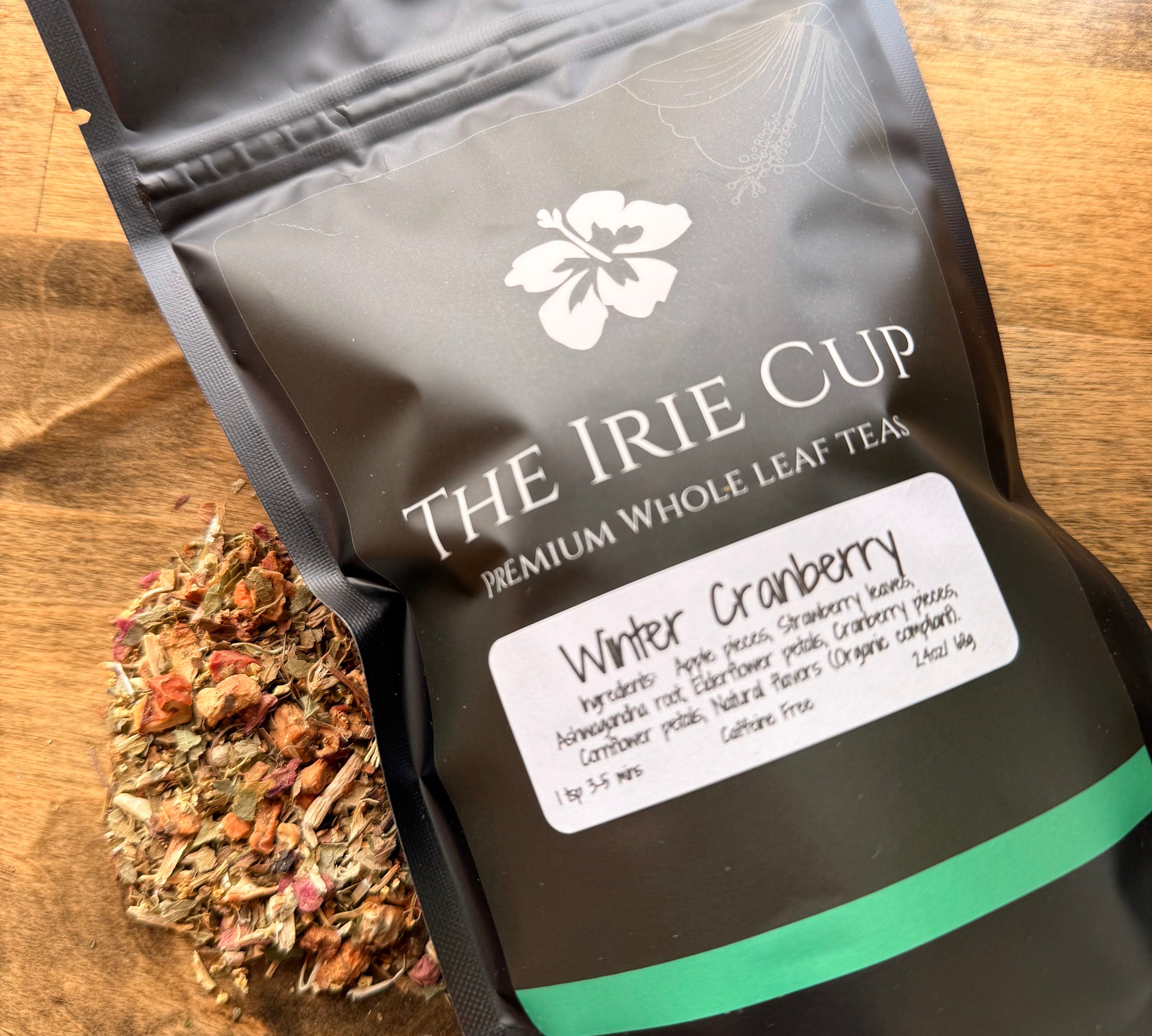 Tea package labeled 'The Irie Cup' with a sample of winter cranberry tea leaves on a wooden surface.