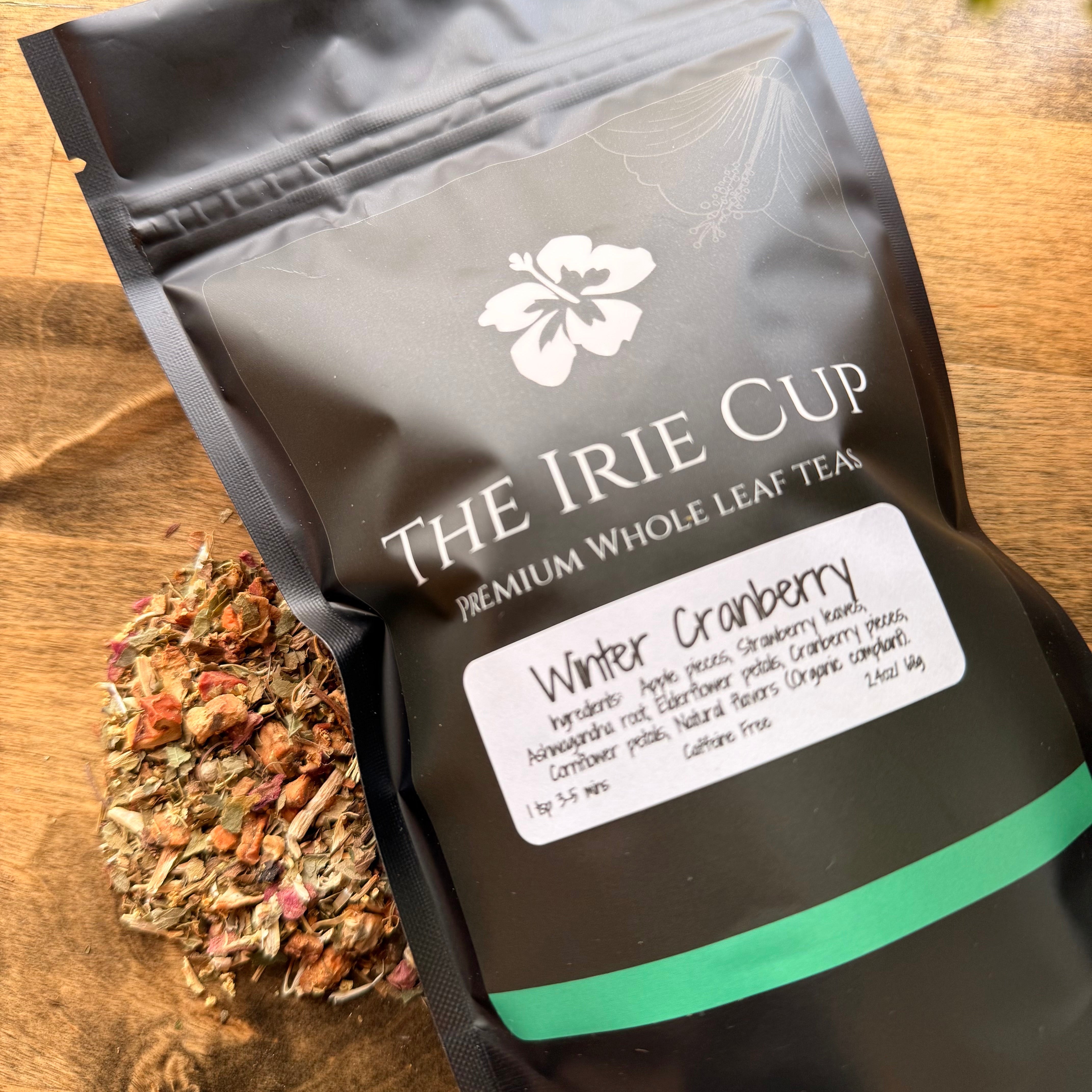 Tea package labeled 'The Irie Cup' with a sample of winter cranberry tea leaves on a wooden surface.