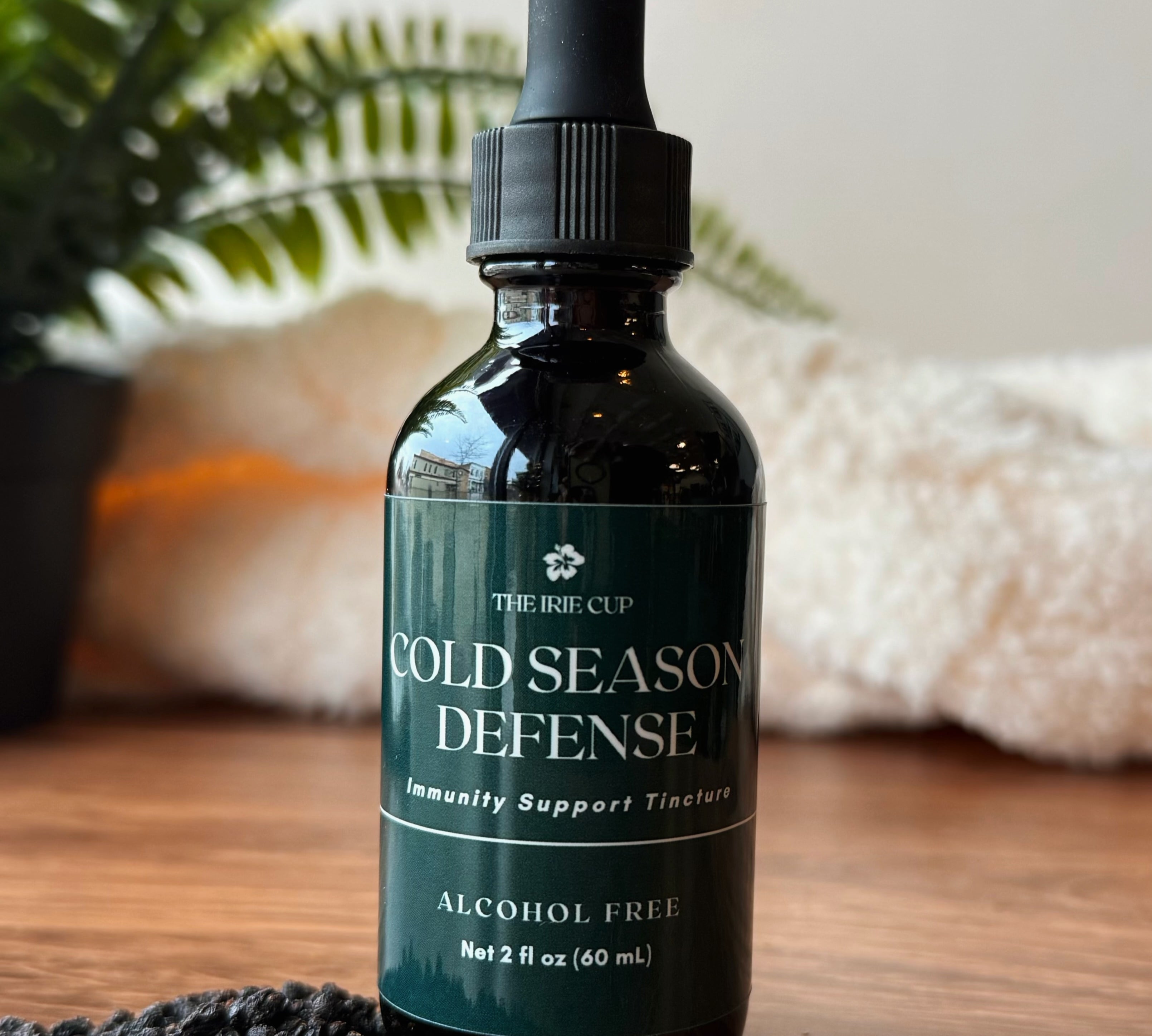 Bottle of 'Cold Season Defense' on a wooden surface with a plant and decorative stones in the background.