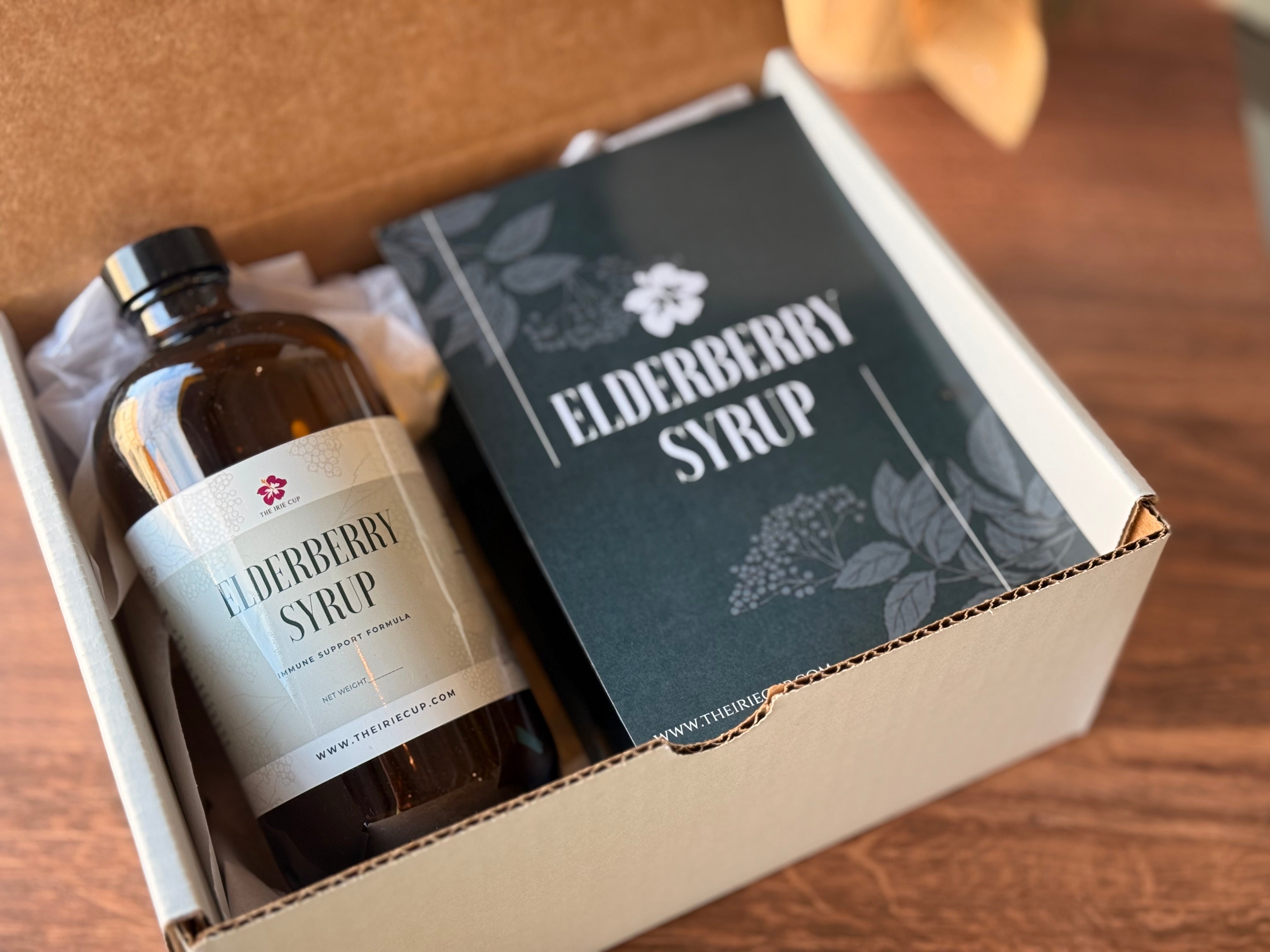 An elderberry syrup kit packaging with a bottle labeled 'Elderberry Syrup' and various herbs, placed on a wooden surface.