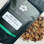 A package of Gentle Senna Herbal Tea by The Irie Cup with loose tea leaves, apple pieces, hibiscus, and rosehips scattered in front.