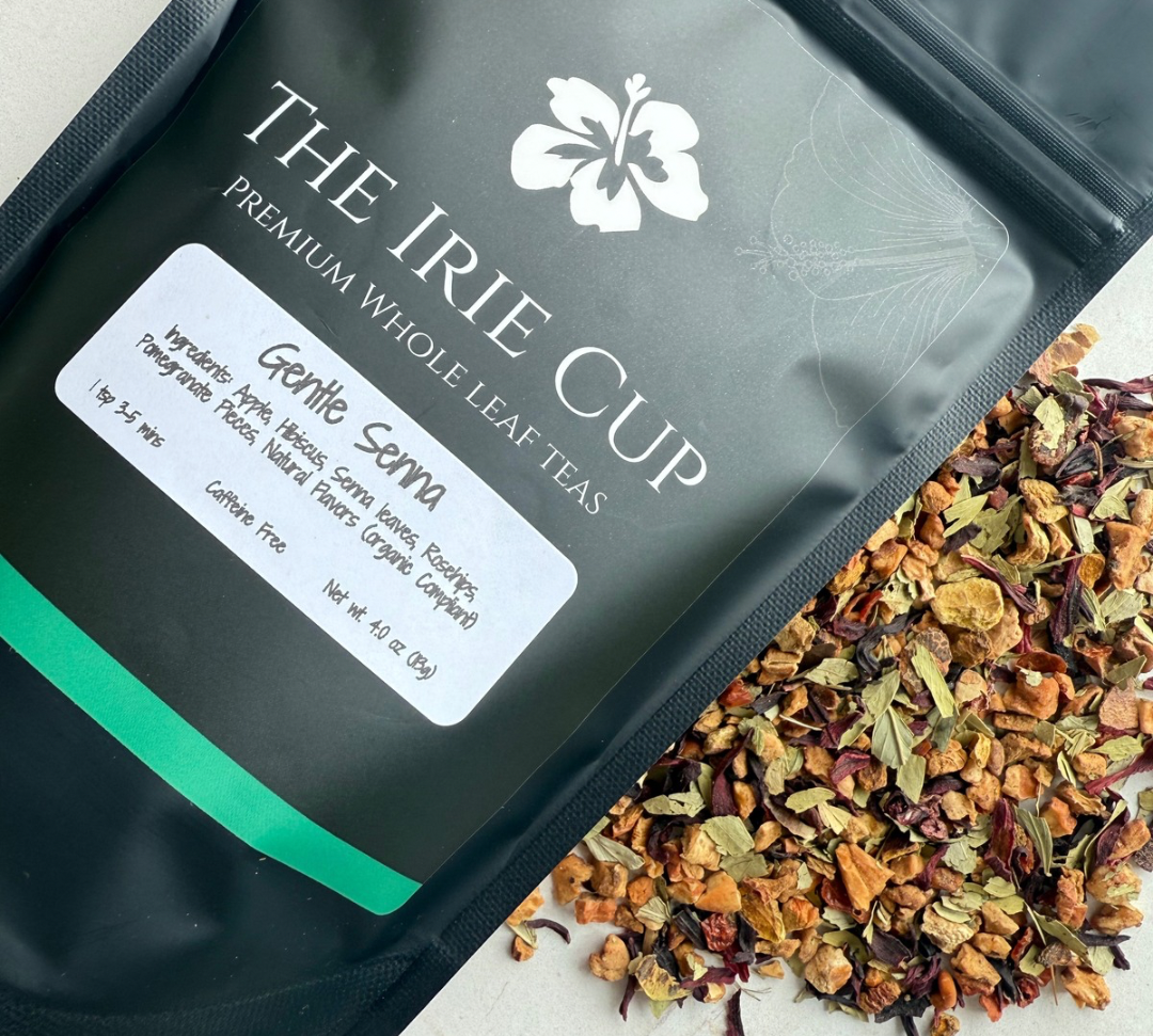 A package of Gentle Senna Herbal Tea by The Irie Cup with loose tea leaves, apple pieces, hibiscus, and rosehips scattered in front.