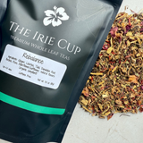 A package of 'The Irie Cup' Rebalance Whole Leaf Tea with its contents spilling out in front, showcasing a mix of dried ginger, licorice, tulsi, dandelion, burdock, rose, and elderflower.
