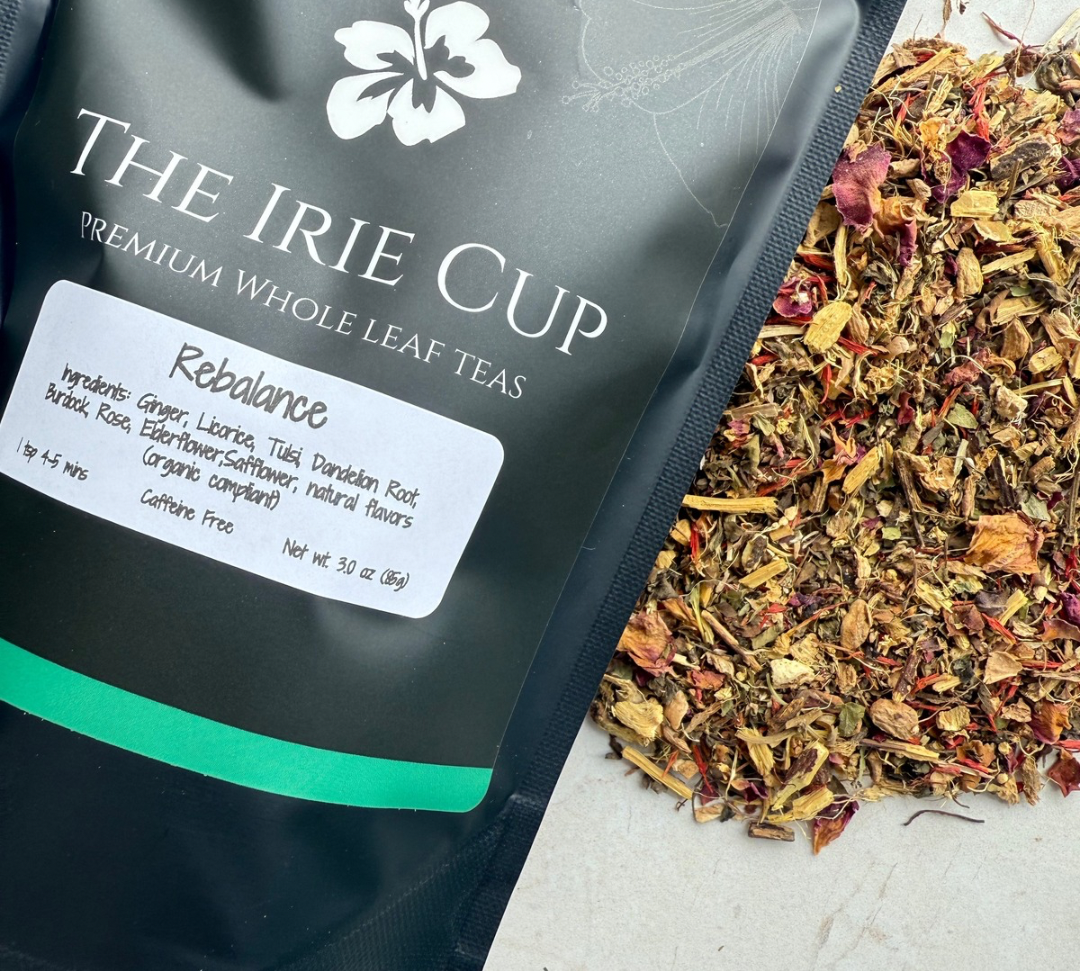 A package of 'The Irie Cup' Rebalance Whole Leaf Tea with its contents spilling out in front, showcasing a mix of dried ginger, licorice, tulsi, dandelion, burdock, rose, and elderflower.