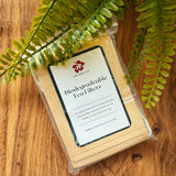 Biodegradable tea filters in a clear package on a wooden surface with fern leaves.
