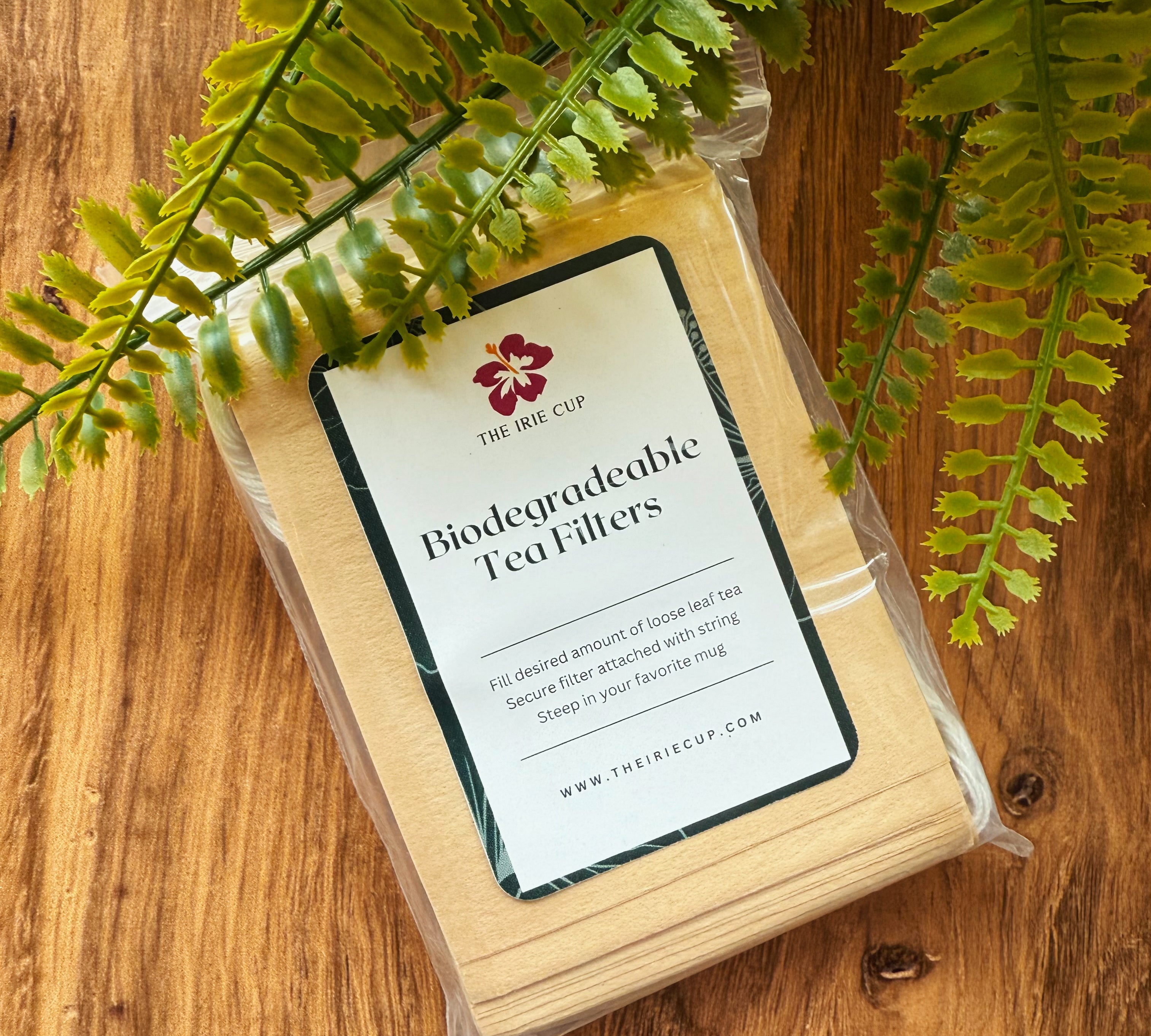 Biodegradable tea filters in a clear package on a wooden surface with fern leaves.