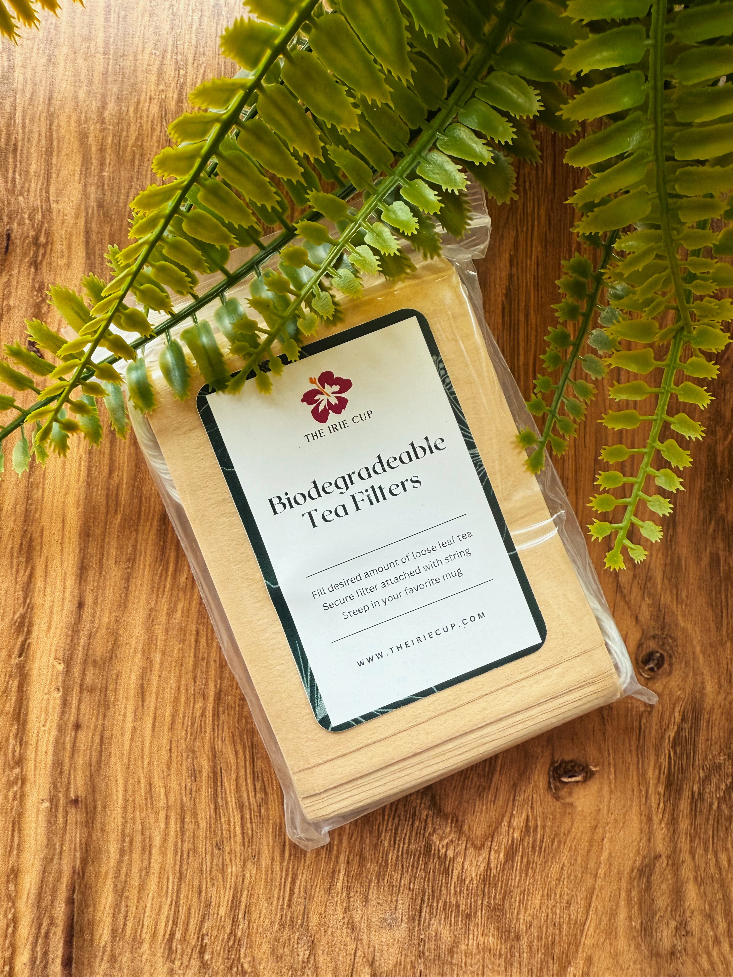 Biodegradable tea filters in a clear package on a wooden surface with fern leaves.