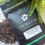 A package of 'The Irie Cup' Pomegranate Hibiscus tea with dried leaves and pieces of pomegranate visible in the foreground.