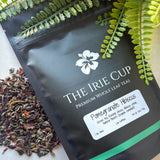 A package of 'The Irie Cup' Pomegranate Hibiscus tea with dried leaves and pieces of pomegranate visible in the foreground.