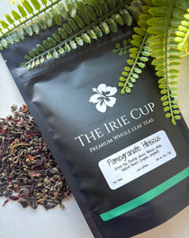 A package of 'The Irie Cup' Pomegranate Hibiscus tea with dried leaves and pieces of pomegranate visible in the foreground.