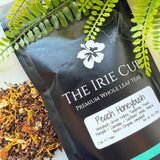 A package of 'The Irie Cup' Peach Honeybush tea with a visible label showing the product name and an image of the tea leaves surrounded by green foliage.