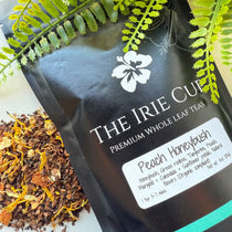 A package of 'The Irie Cup' Peach Honeybush tea with a visible label showing the product name and an image of the tea leaves surrounded by green foliage.