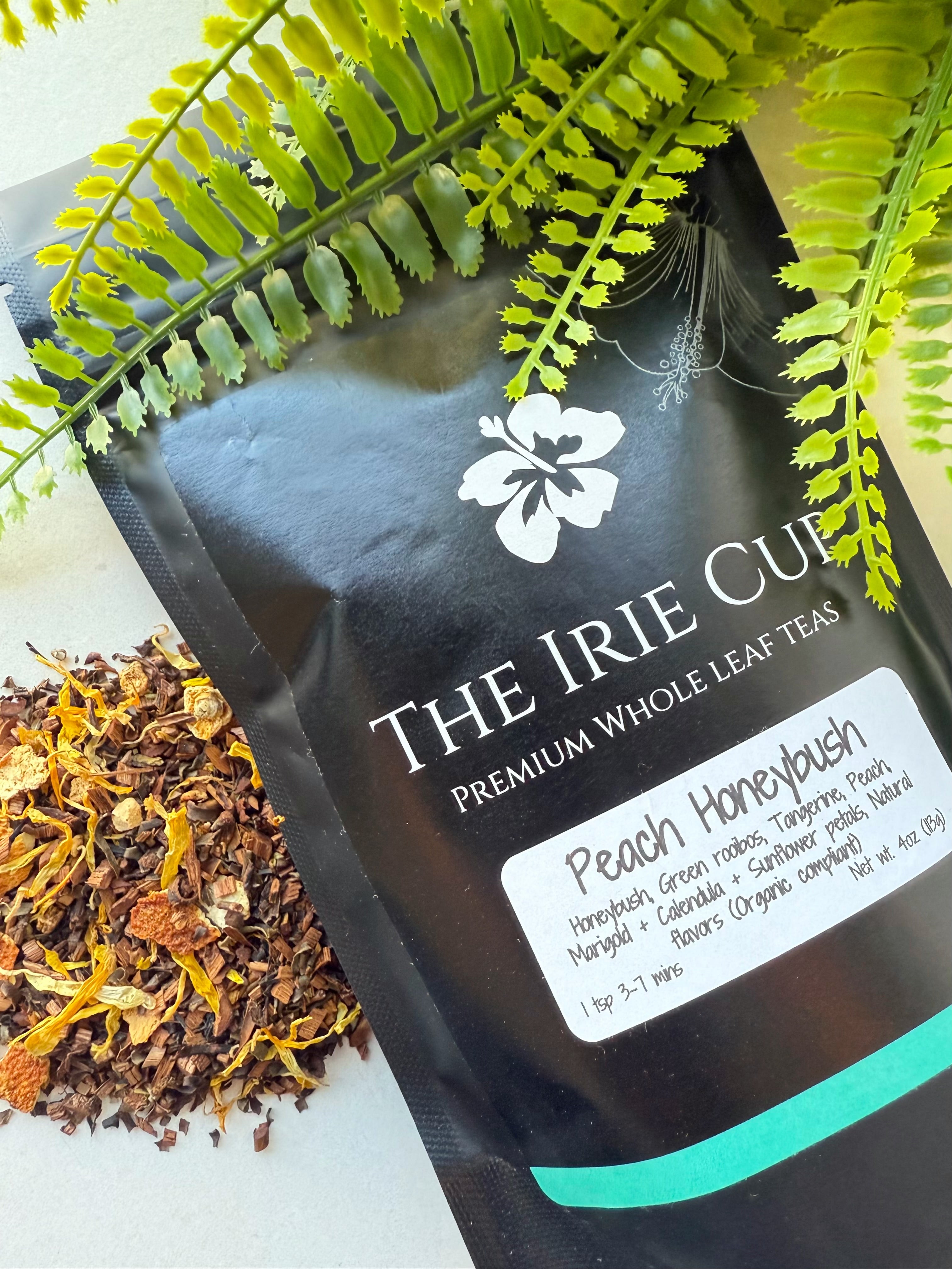 A package of 'The Irie Cup' Peach Honeybush tea with a visible label showing the product name and an image of the tea leaves surrounded by green foliage.