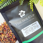A package of 'The Irie Cup' Raspberry Lemonade tea with loose tea leaves and pieces of raspberry and hibiscus visible in the foreground.