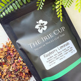 A package of 'The Irie Cup' Raspberry Lemonade tea with loose tea leaves and pieces of raspberry and hibiscus visible in the foreground.