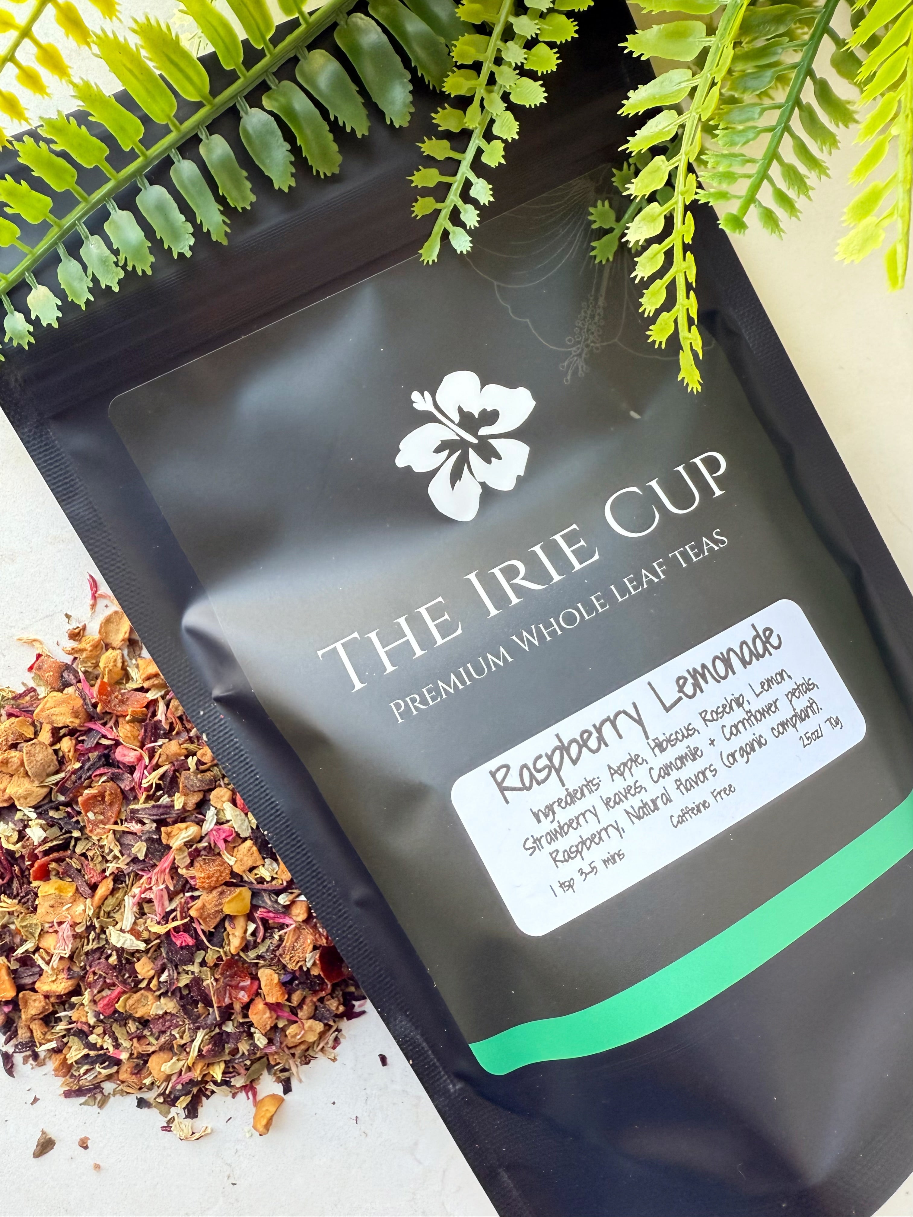 A package of 'The Irie Cup' Raspberry Lemonade tea with loose tea leaves and pieces of raspberry and hibiscus visible in the foreground.