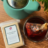 Tea set with a teapot, glass mug with tea, and a package of tea filters on a wooden surface.