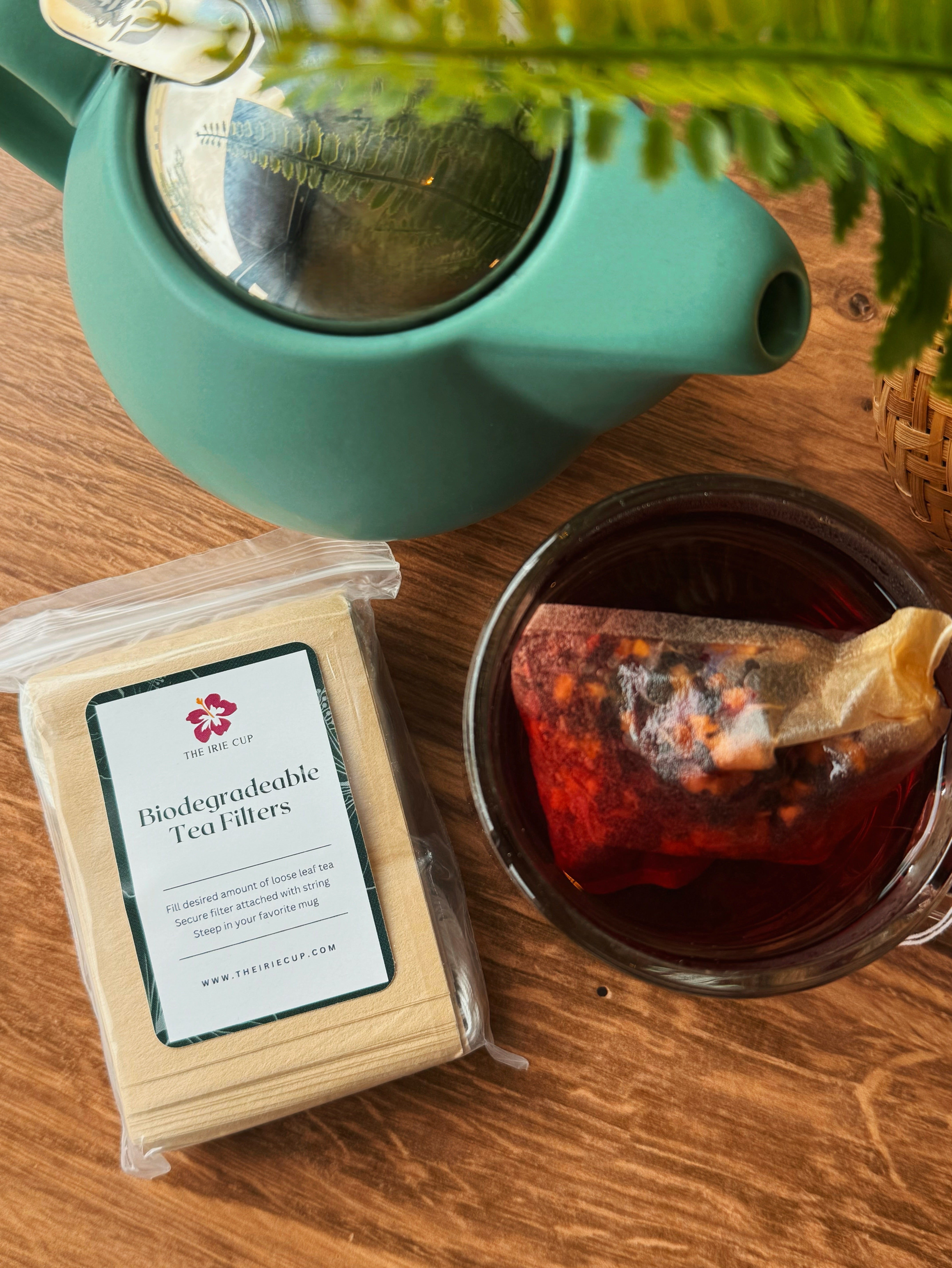 Tea set with a teapot, glass mug with tea, and a package of tea filters on a wooden surface.